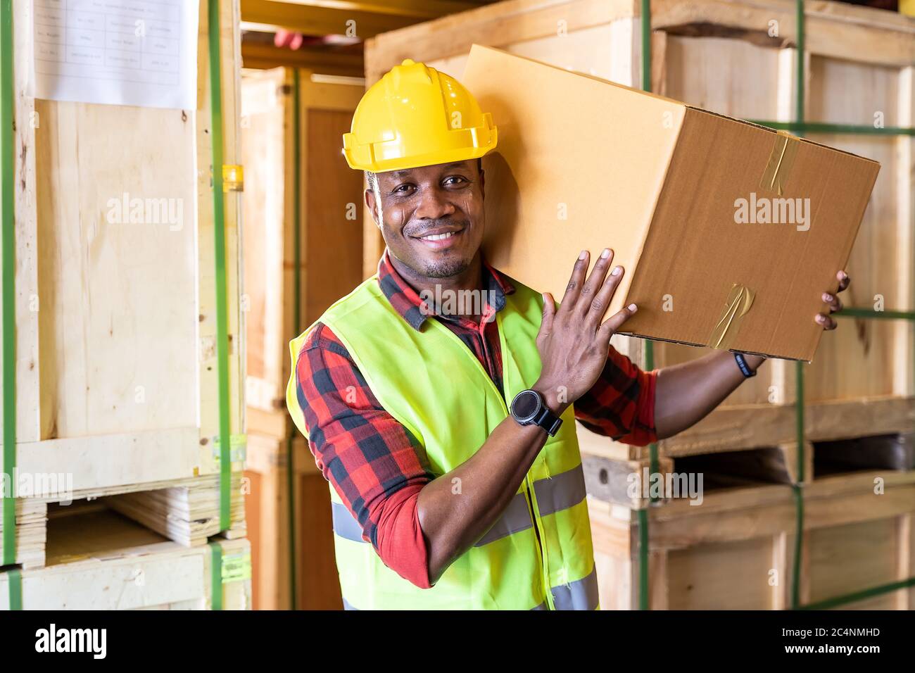 Portrait des afrikanischen schwarzen Lagerarbeiters Halten Sie Kartonverpackungen auf seiner Schulter in großen Lagerverteilerzentren. Verwenden in b Stockfoto