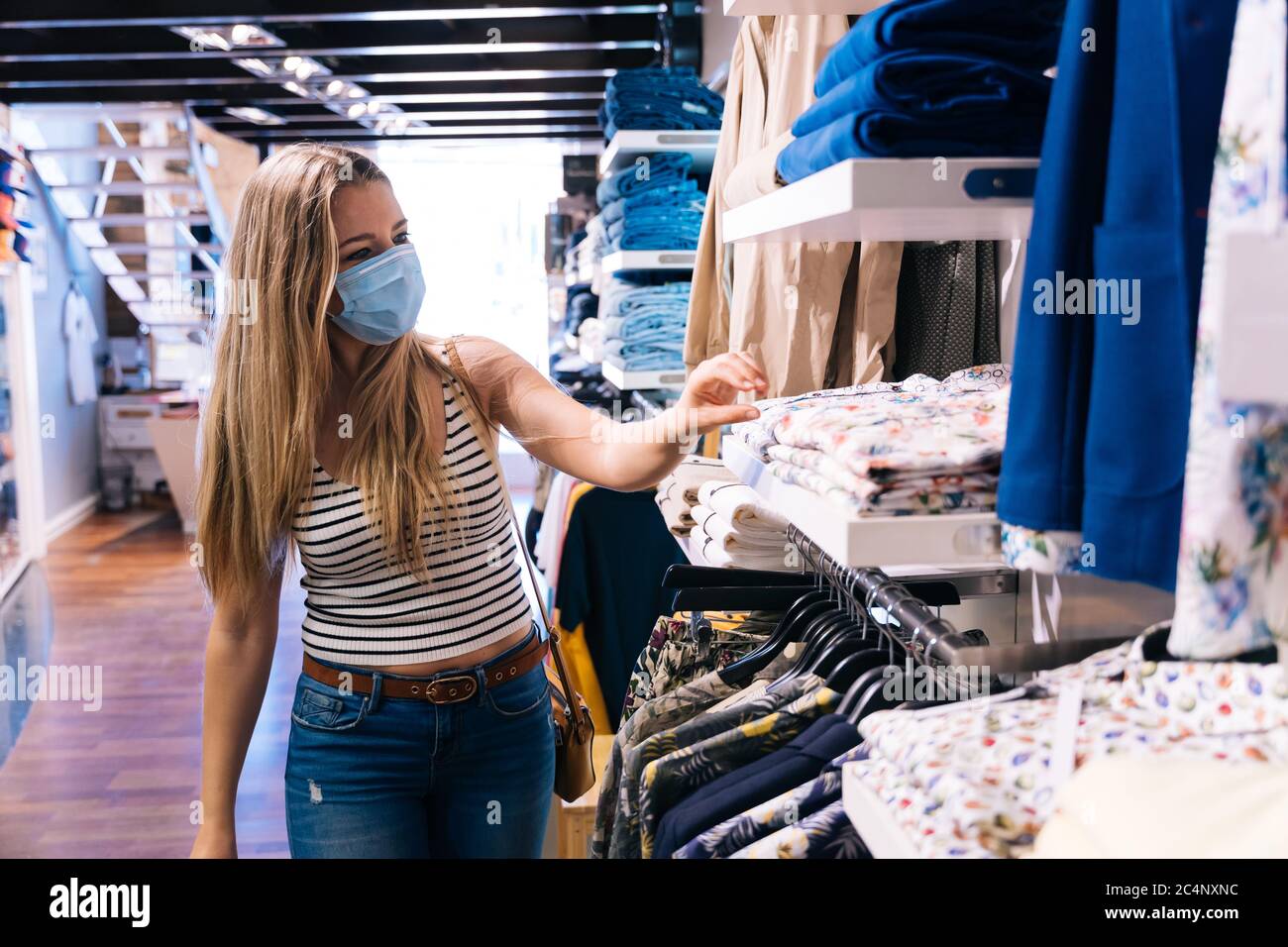Junge Frau in Maske einkaufen in einem Bekleidungsgeschäft in der Coronavirus-Pandemie Stockfoto
