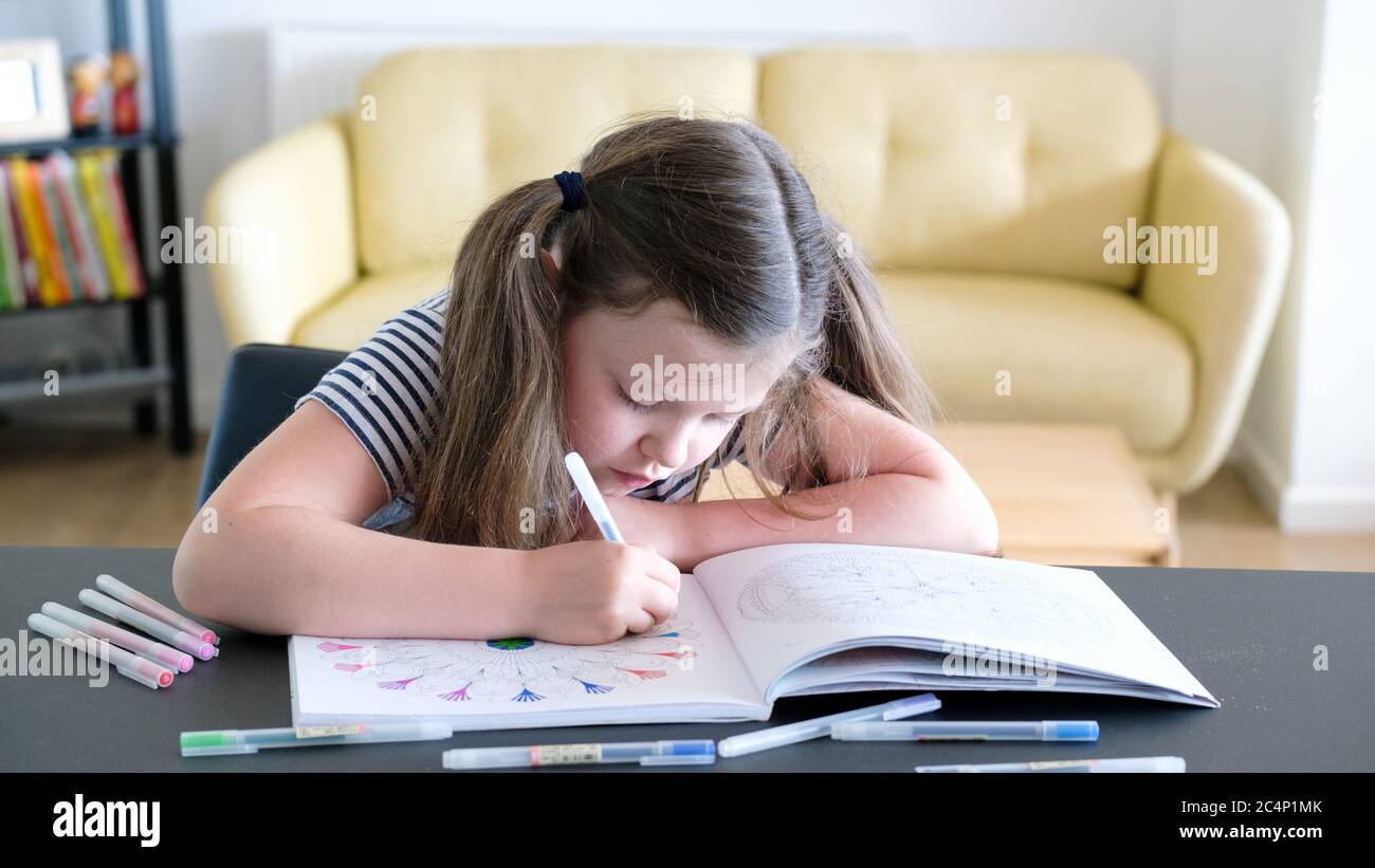 Ein Kind saß zu Hause und konzentrierte harte Färbung in einem Erwachsenen Malbuch mit verschiedenen farbigen Stiften Stockfoto