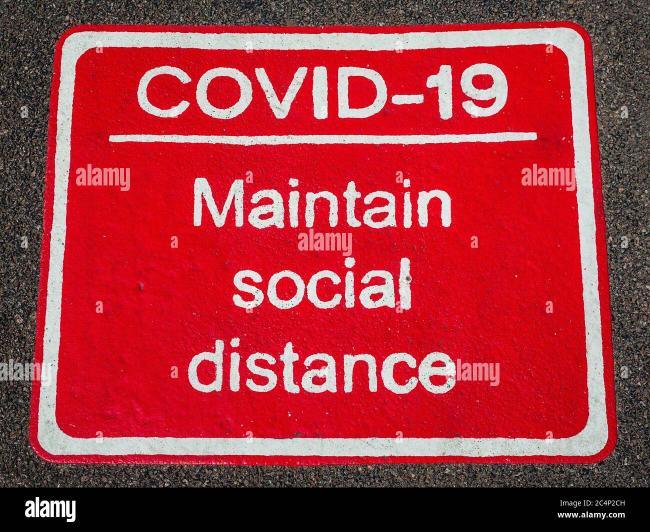 Covid-19 Pflegen Sie soziale Distanz Straße und Bürgersteig Zeichen in Großbritannien. Coronavirus Pflegen Soziale Distanz Pflaster Zeichen. Stockfoto
