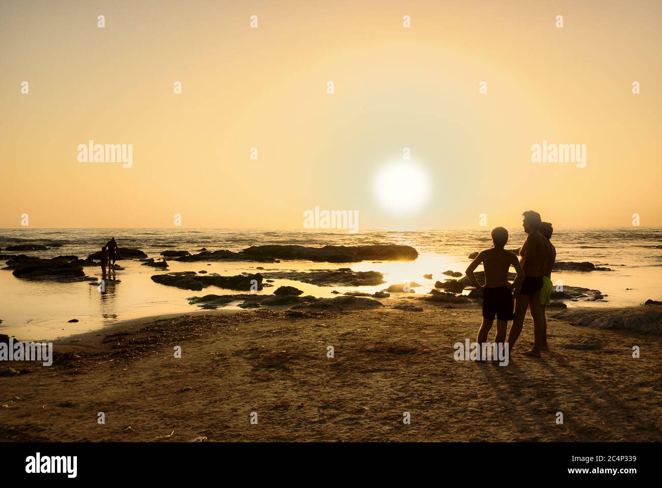 Vater und Söhne genießen den Blick auf den Sonnenuntergang auf dem Meer von Sizilien in Sommerferien Stockfoto