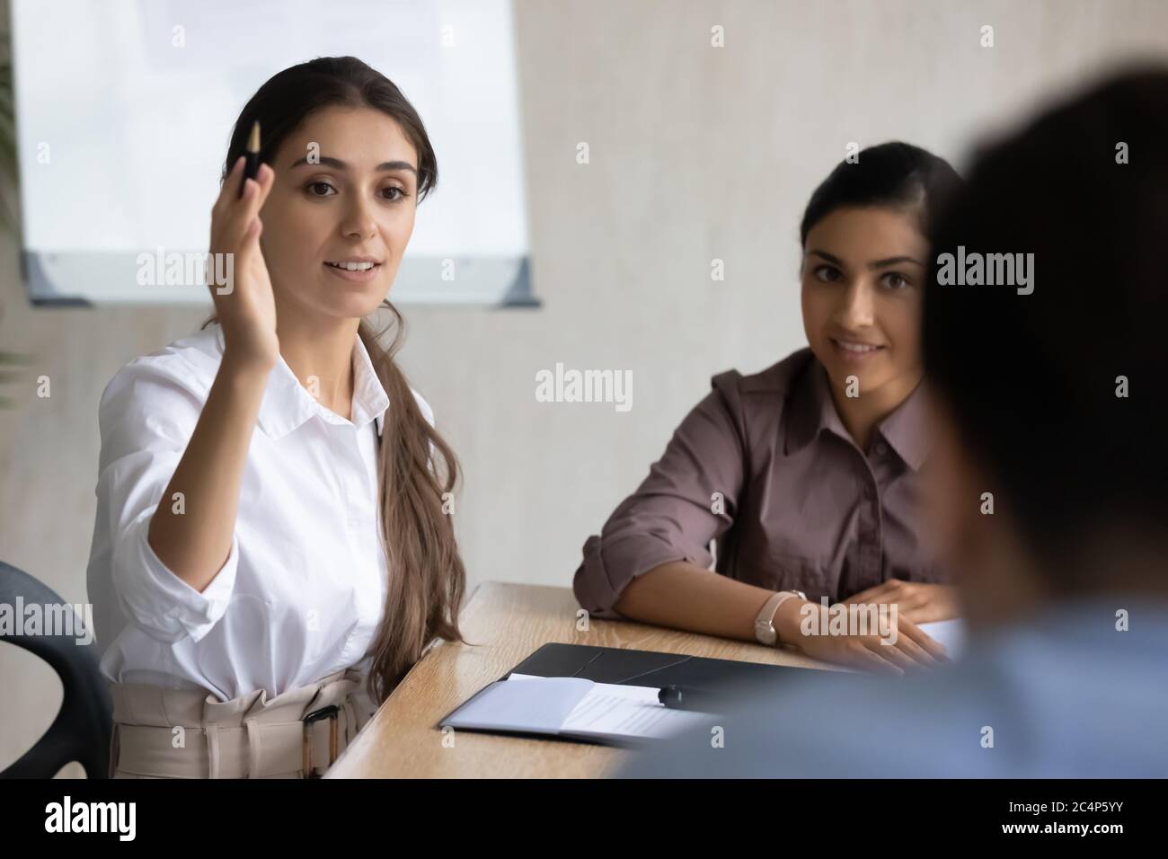 Lächelnde arabische Geschäftsfrau, die Hand hebt und Frage an Mentor stellt Stockfoto