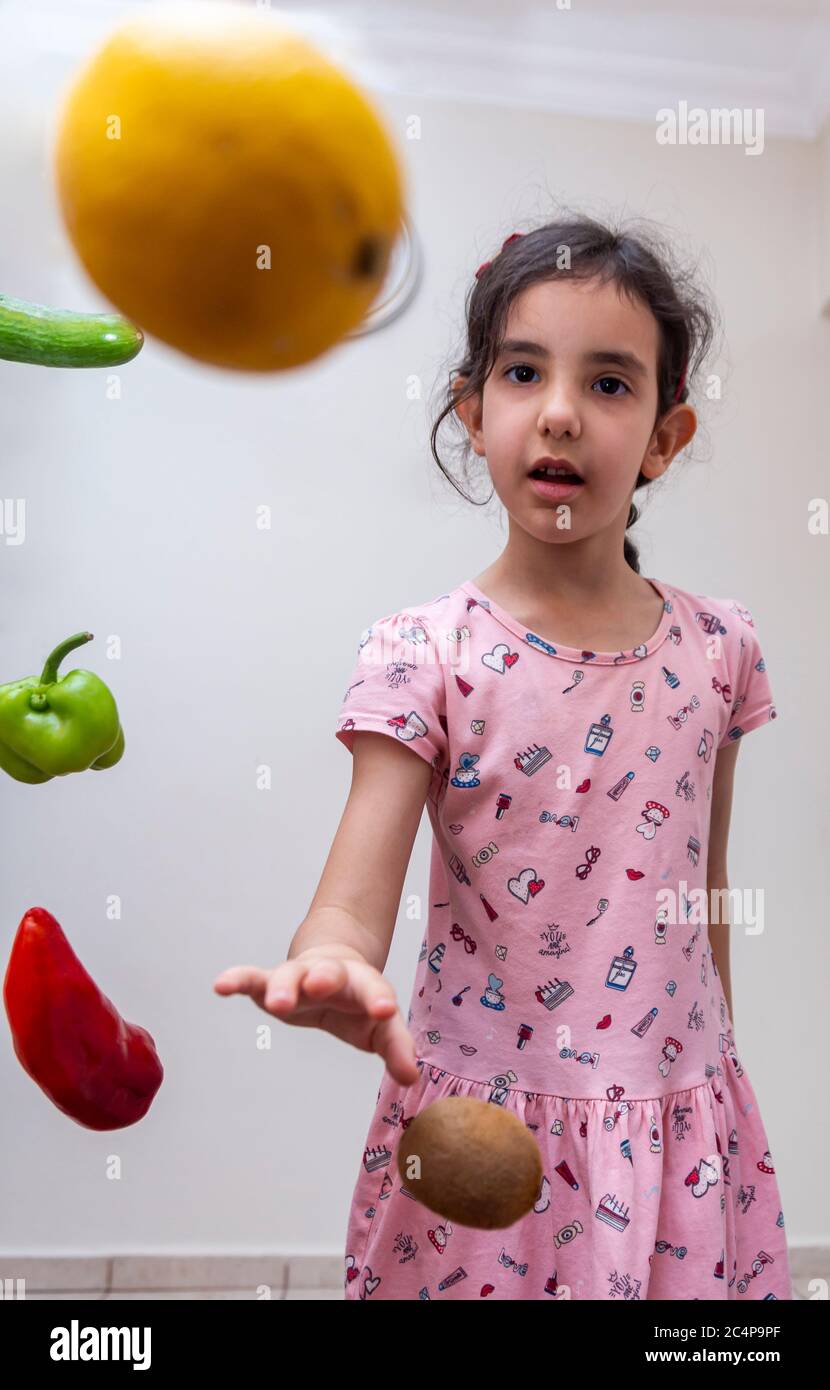 Ein kleines Mädchen spielt mit umgebenem Gemüse bei sich zu Hause Stockfoto
