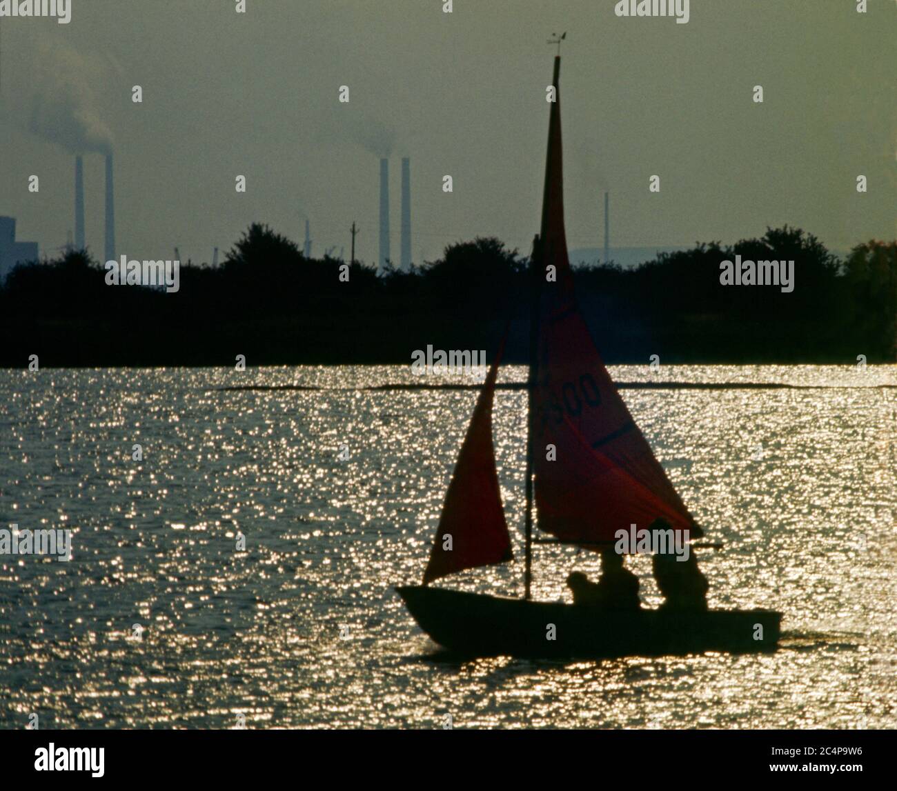 Kleine Yacht segelt am späten Nachmittag, gesehen vor einem industriellen Hintergrund, Kent, England Stockfoto