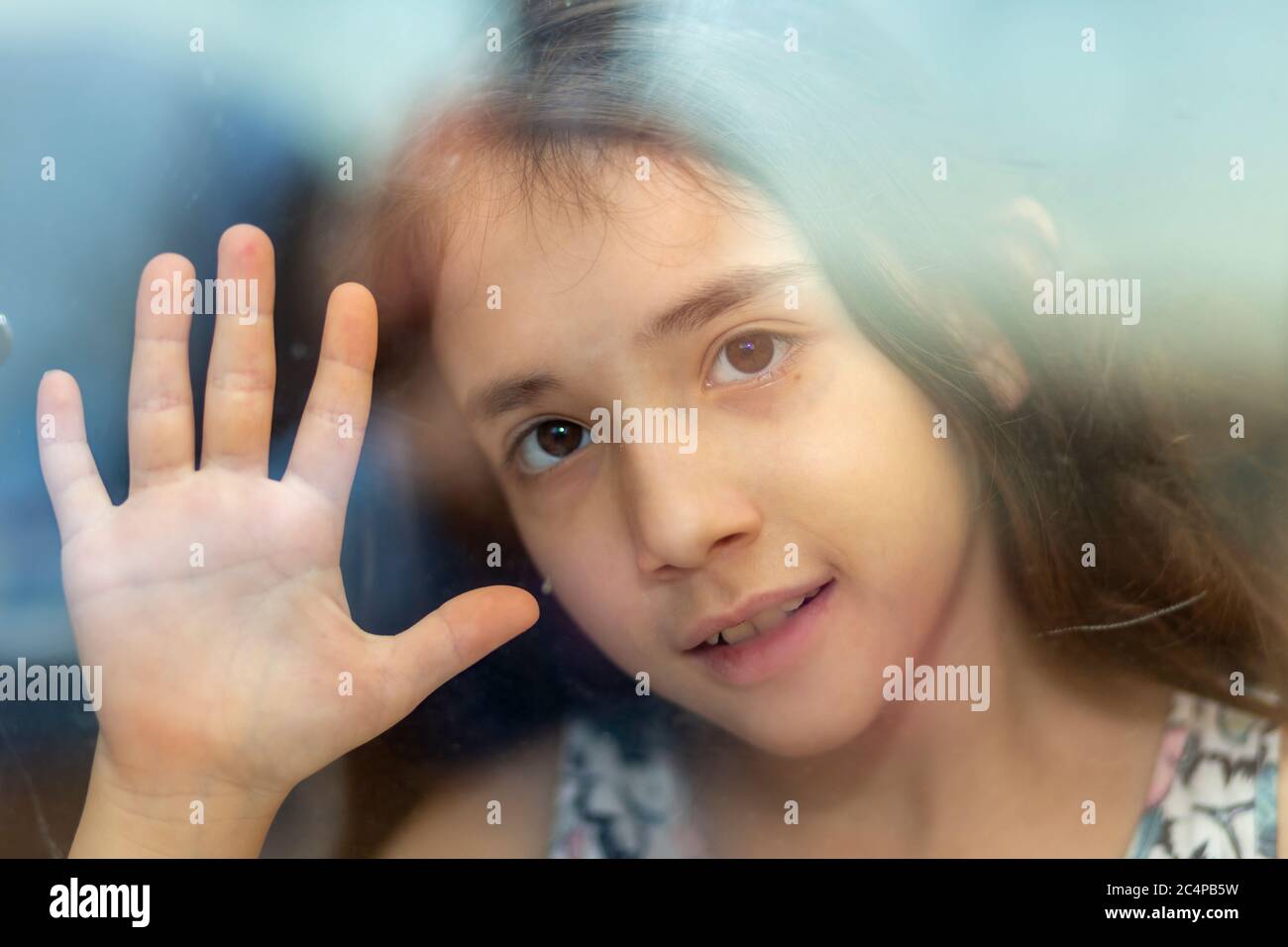 Hinter dem Fenster wartet sie auf sie. Ein glückliches lächelndes kleines Mädchen legte Ihre Hände auf die Fenster während Corona Quarantäne Stockfoto