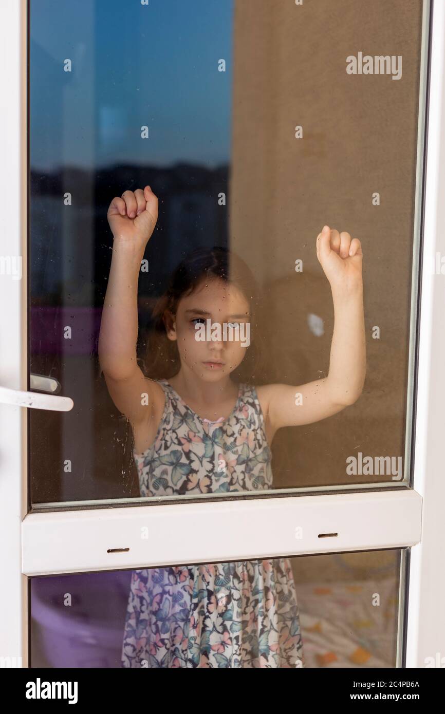 Unglücklich und gelangweilt kleines Mädchen wartet hinter der Garten Glastür. . Ein gelangweiltes und depressiv kleines Mädchen legte ihre Hände während der Corona an die Fenster. Stockfoto