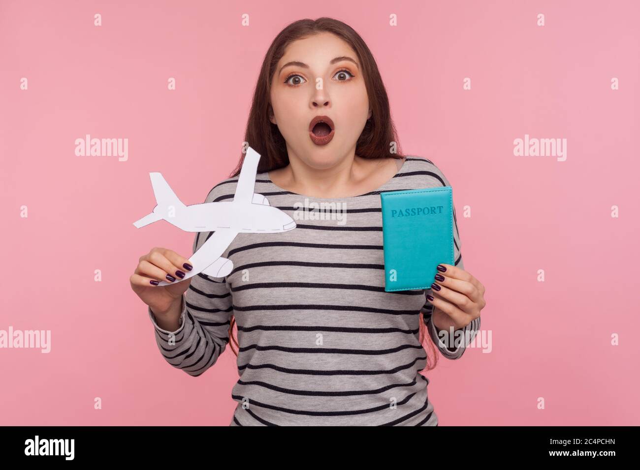 Wow, ich werde auf Reise gehen! Portrait von staunenden schönen jungen Frau hält Pass und Papier Flugzeug, Blick auf die Kamera mit überraschter Ausdruck, sho Stockfoto