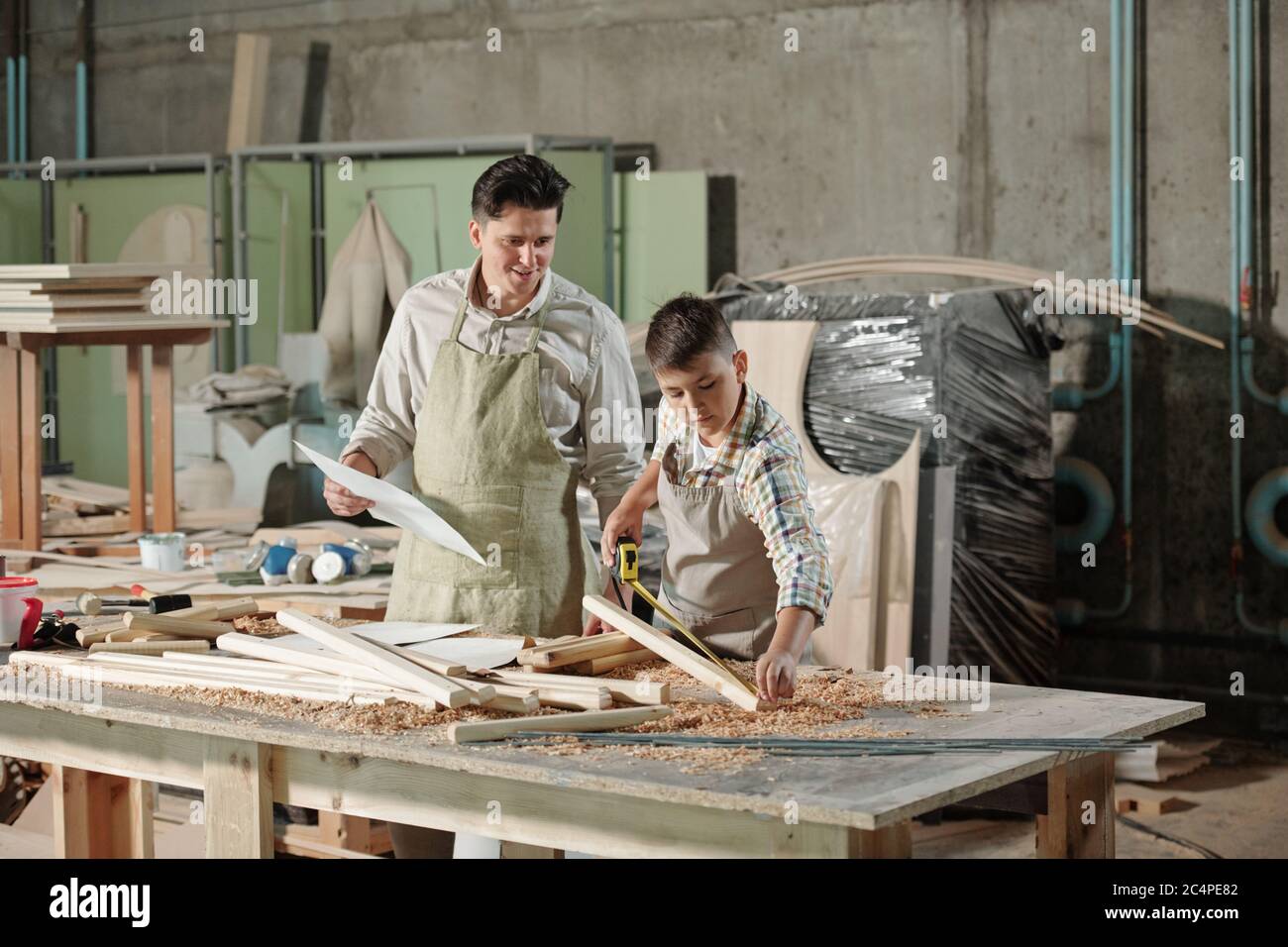 Inhalt zufrieden Vater mit Skizze Blick auf Teenager-Sohn messen Holzbrett in Holzbearbeitung Studio Stockfoto