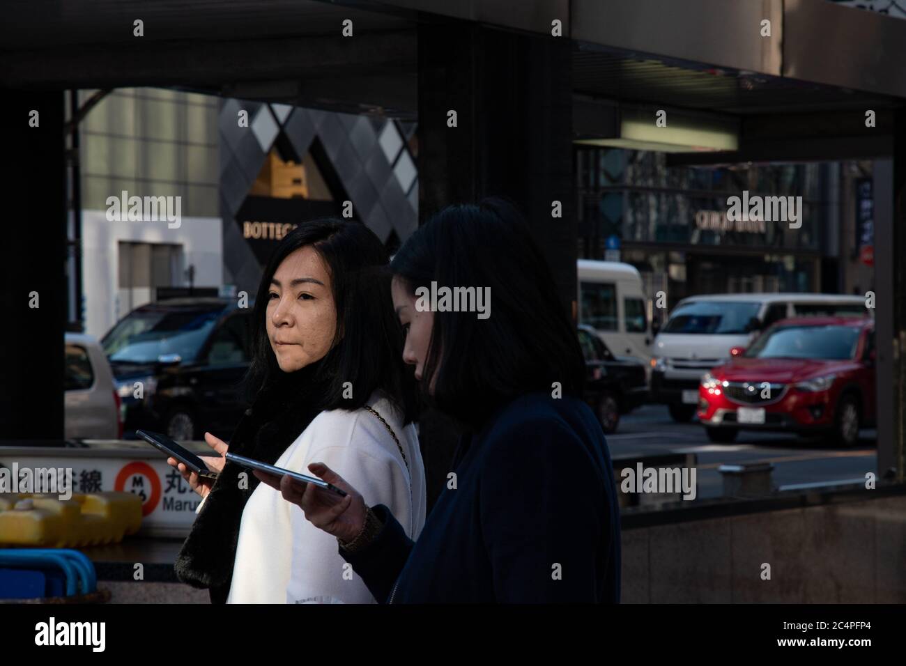 Straßenfotografie von zwei jungen japanischen Freundinnen in Ginza. U-Bahn-Station, Autos und Boutiquen im Hintergrund. Tokio, Japan. Stockfoto