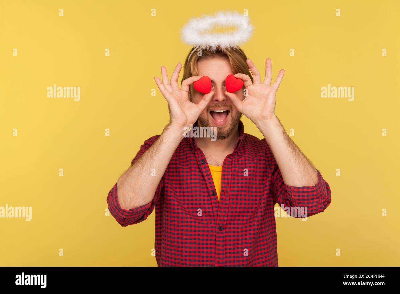 Lustige bärtige Kerl saint Halo Abdeckung Augen mit Spielzeug Herzen als ob mit Liebe suchen, Ausdruck romantische Gefühle, Zuneigung Anbetung in Beziehungen. In Stockfoto