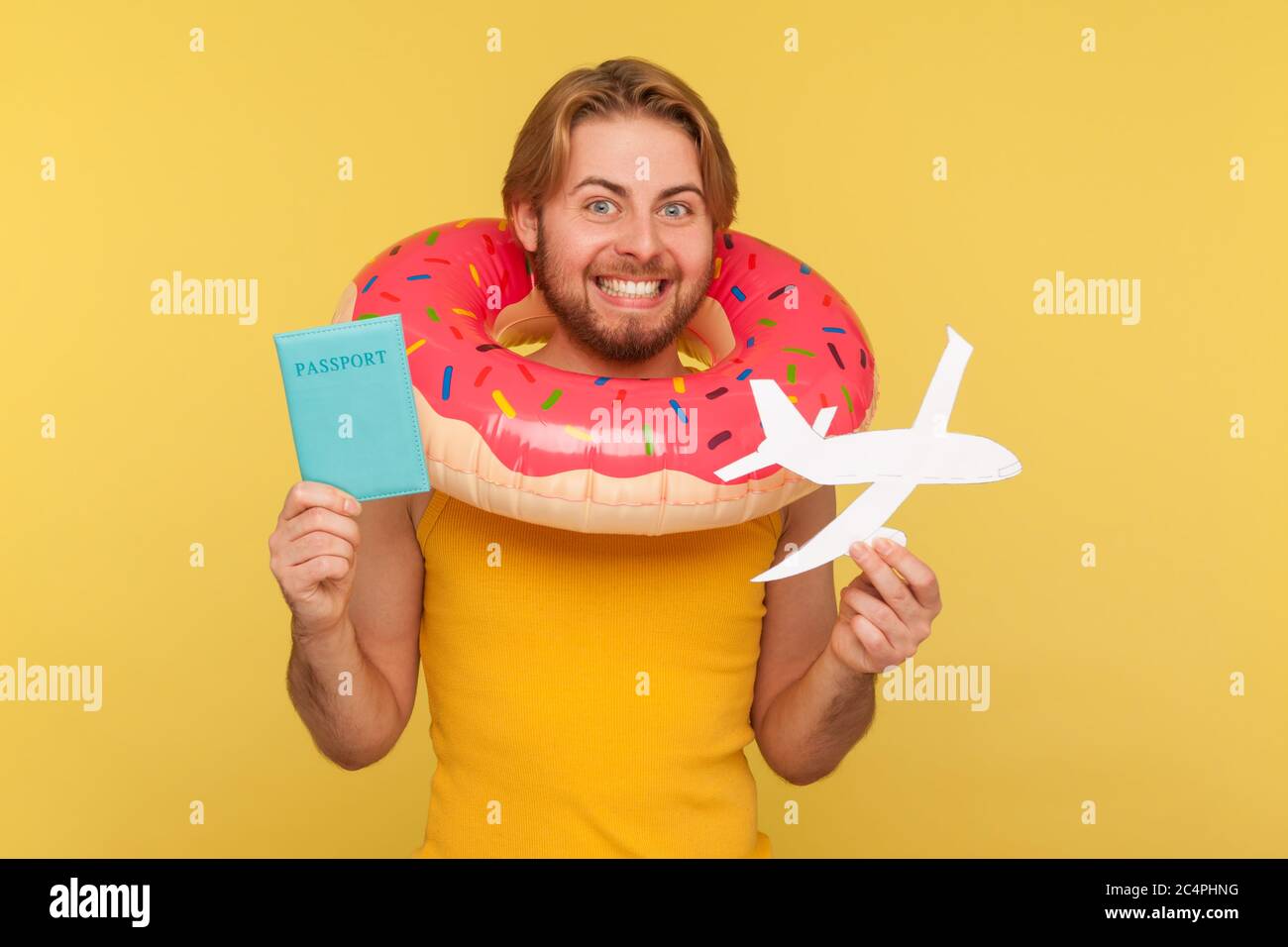 Aufgeregt optimistisch lustige Tourist Kerl in Unterhemd stehen mit rosa Donut Gummiring, halten Passdokument und Flugzeug-Mockup, jubelte Reise Stockfoto