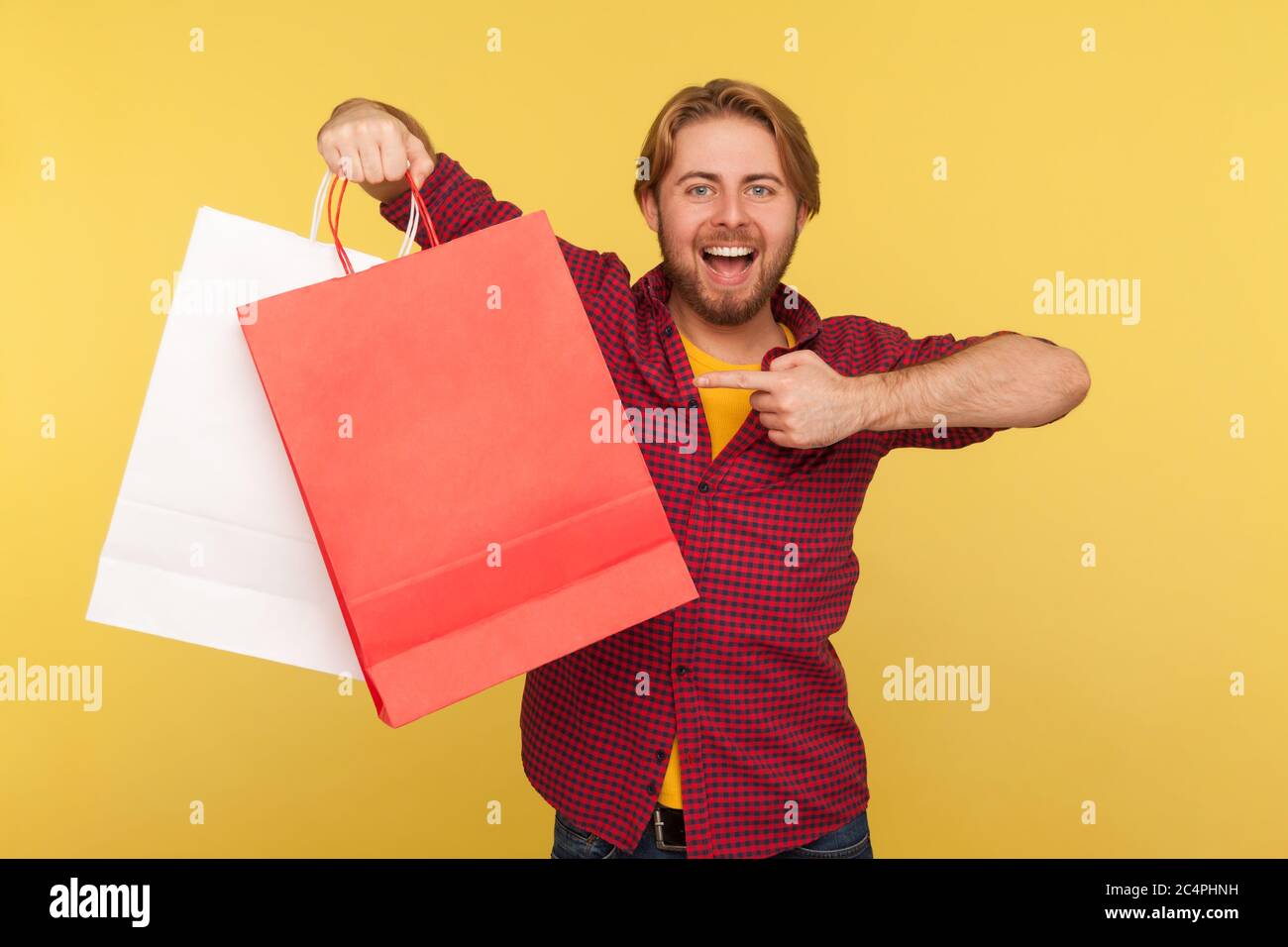 Happy Shopper, schöner stilvoller Kerl in karierten Hemd zeigt Einkaufstaschen blank Modell bis Paket, Blick auf Kamera mit Aufregung toothy Lächeln. ich Stockfoto