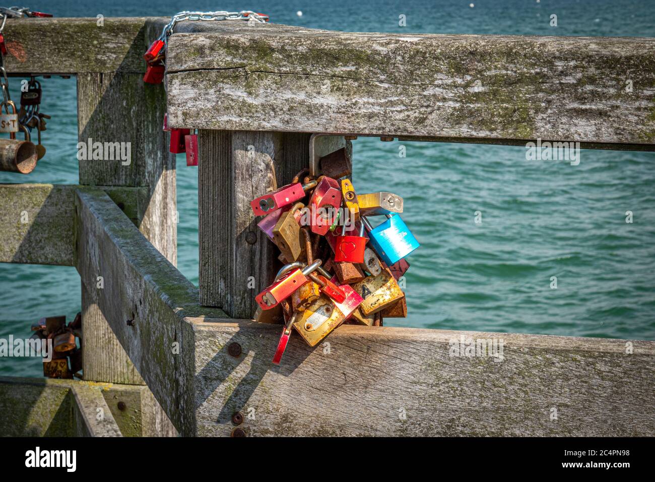 Verschiedene farbige Vorhängeschlösser hängen als Bündel an einem Holzgeländer Stockfoto