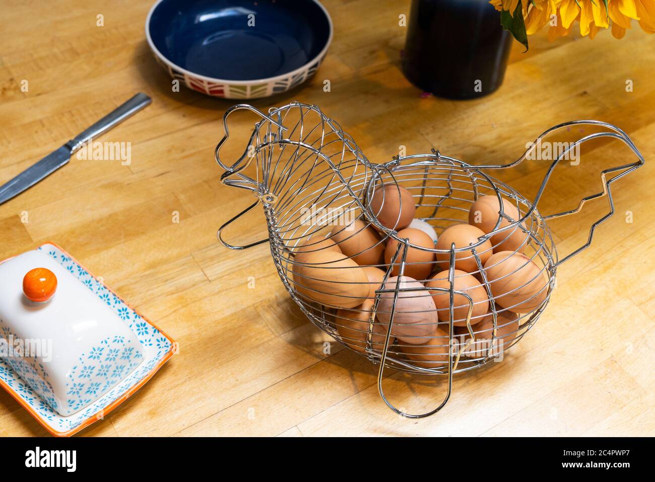 Ein Drahtkorb in Hühnerform, der Hühnereier auf einem hölzernen Frühstückstisch hält, Großbritannien Stockfoto