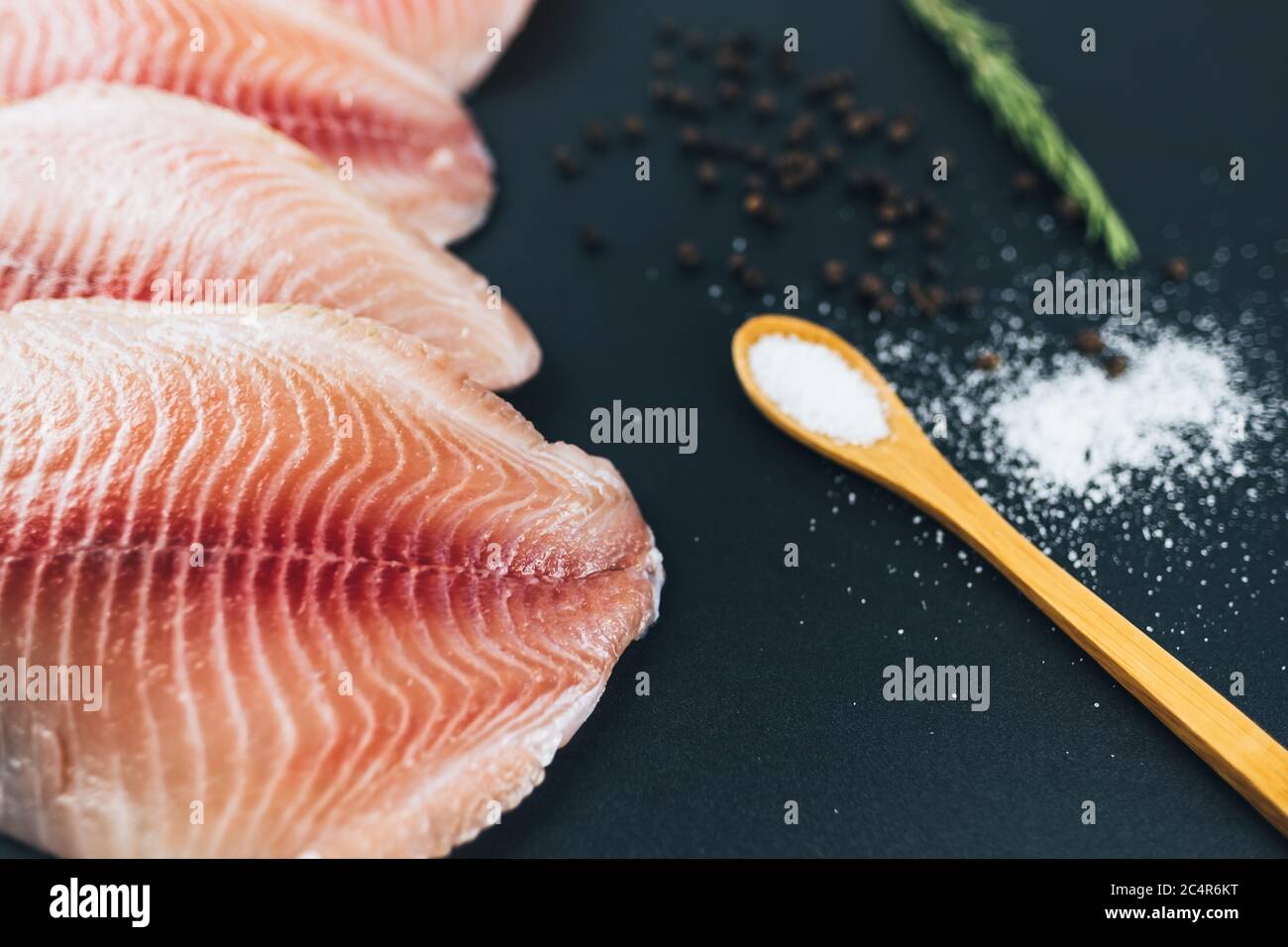 Frisches Filet aus weißem Tilapia-Fisch vor schwarzem Hintergrund. Stockfoto