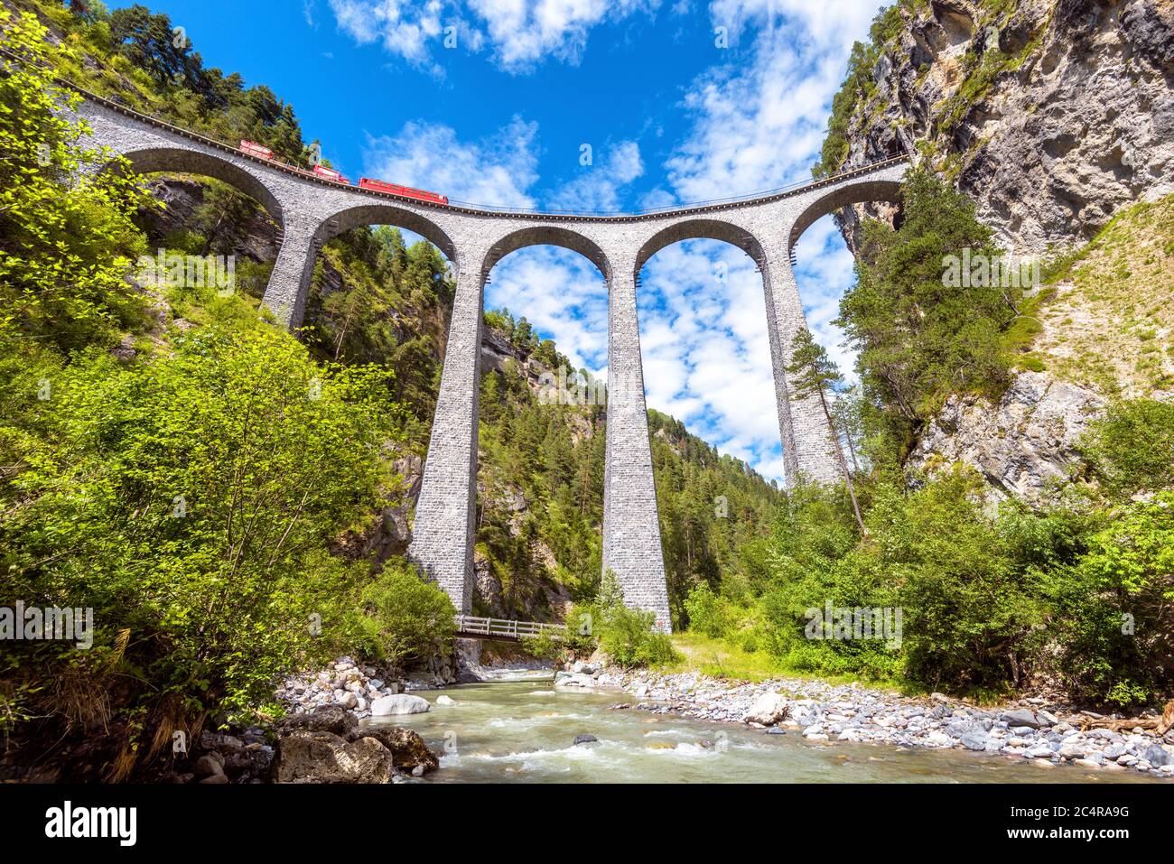 Landwasser Viadukt über Fluss, Filisur, Schweiz. Es ist Wahrzeichen der Schweizer Alpen. Rote Bahn fährt auf hoher Eisenbahnbrücke in den Bergen. Landschaftlich schöner Blick auf Stockfoto