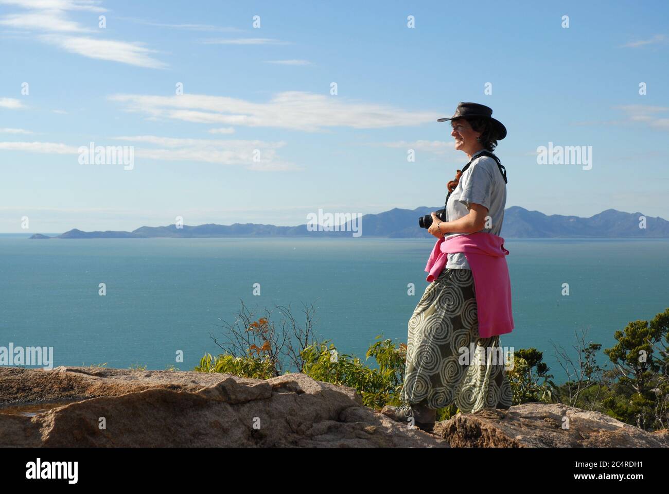 Frau, die auf Granitfelsen auf dem Gipfel des Forts Walk steht und mit Cape Cleveland am Horizont, Magnetic Island, Queensland, aufs Meer blickt Stockfoto