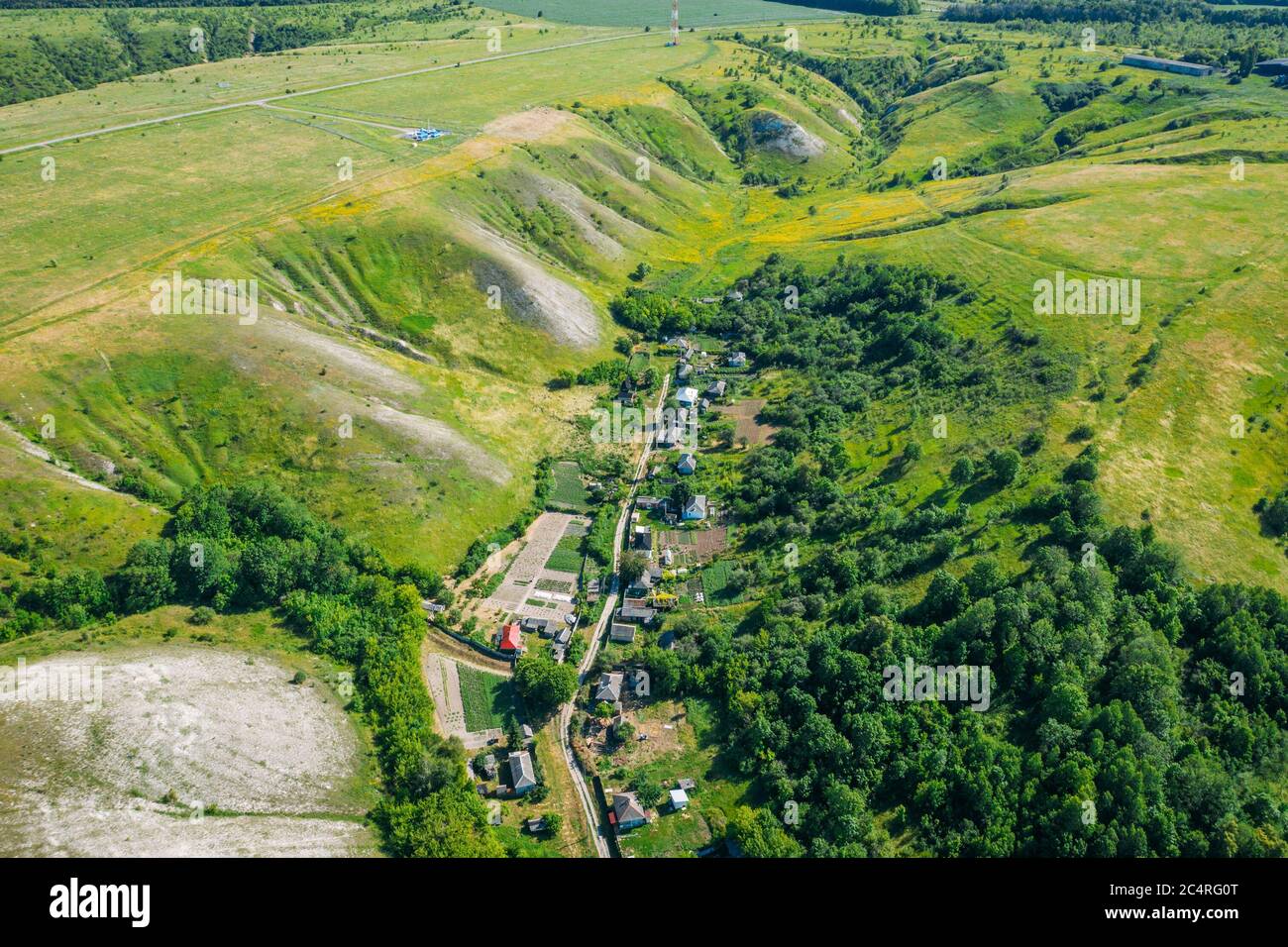 Ländliche Dorf zwischen grünen Hügeln und landwirtschaftlichen Feldern in der Landschaft, Luftbild von Drohne. Stockfoto