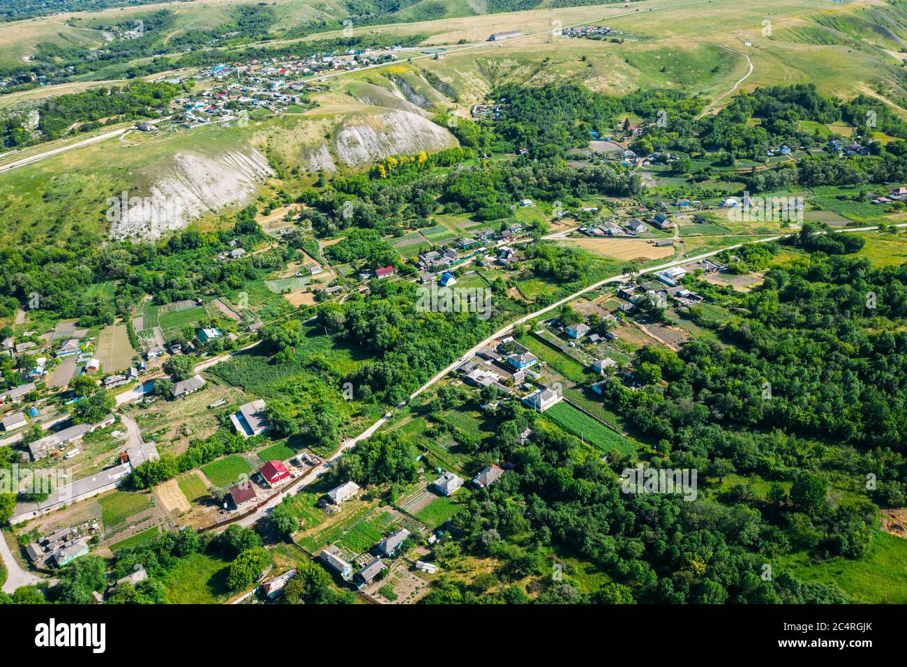 Ländliche Dorf zwischen grünen Hügeln und landwirtschaftlichen Feldern in der Landschaft, Luftbild von Drohne. Stockfoto