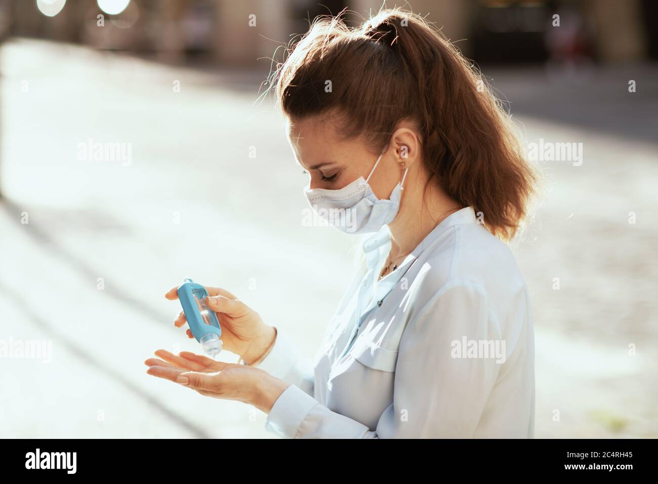 Leben während der Coronavirus-Pandemie. Junge Frau in blauer Bluse mit medizinischer Maske Desinfektion Hände mit Desinfektionsmittel im Freien in der Stadt. Stockfoto