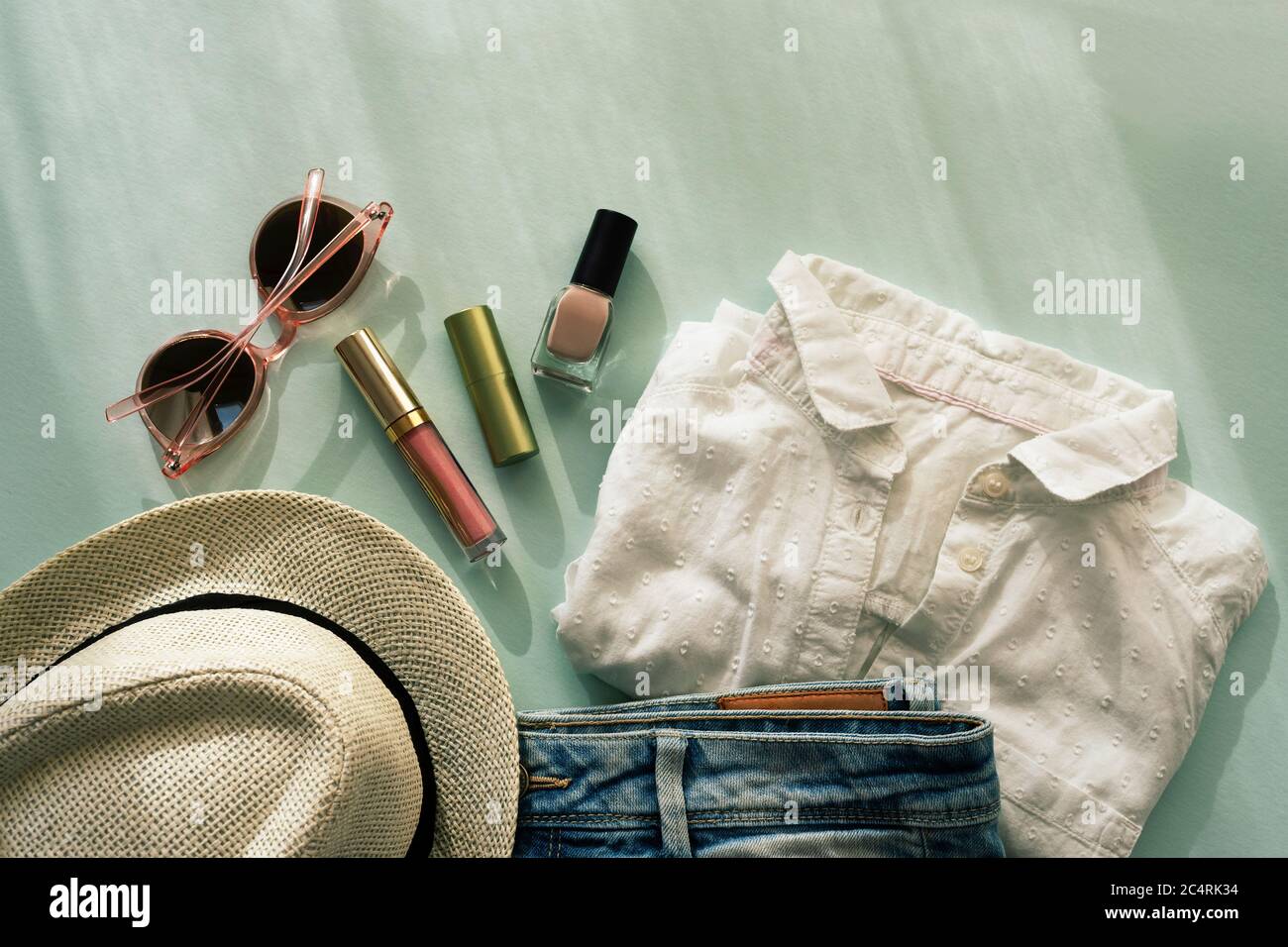 Damen Sommer Mode Accessoires, Hut, Sonnenbrille, Shorts, T-Shirt, Kosmetik in Sonnenlicht mit Schatten. Draufsicht, flach liegend. Stockfoto