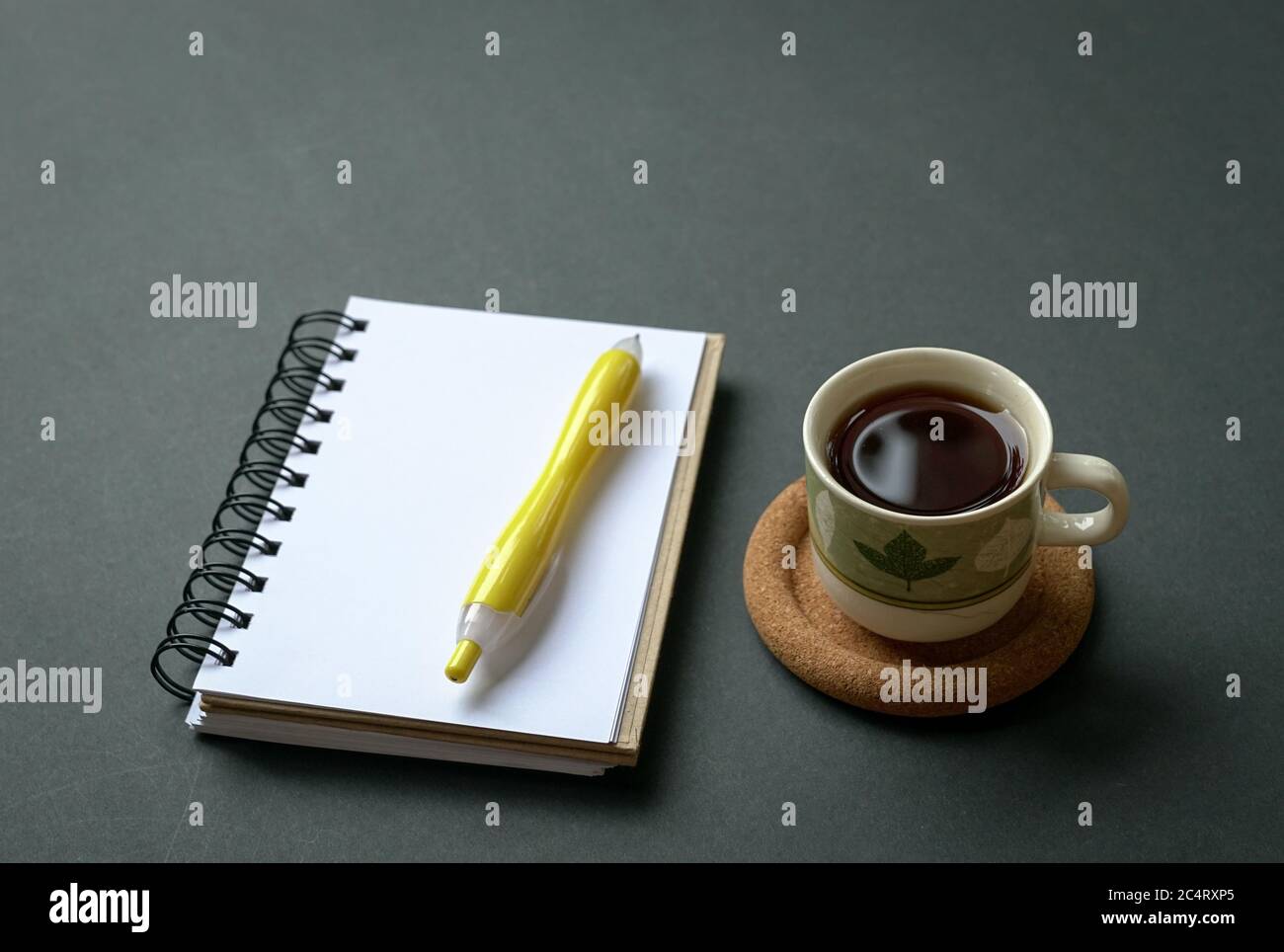 Kaffeetasse mit Notizblock und Stift auf rustikalem schwarzen Tisch. Draufsicht mit Kopierbereich. Stockfoto