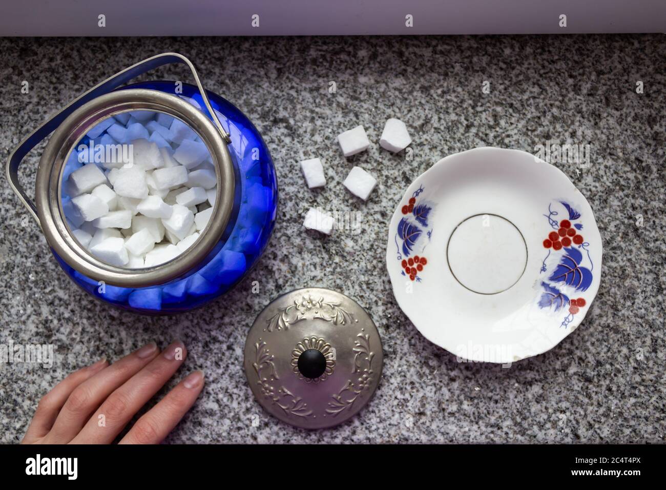 Die weibliche Hand hält eine Zuckerschüssel, in der der Zucker liegt Stockfoto