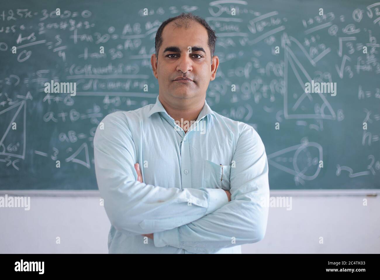 Portrait von ernsthaften männlichen Lehrer, der gegen Tafel steht und Mathematik im Klassenzimmer, Schule und Bildungskonzept unterrichtet. Stockfoto