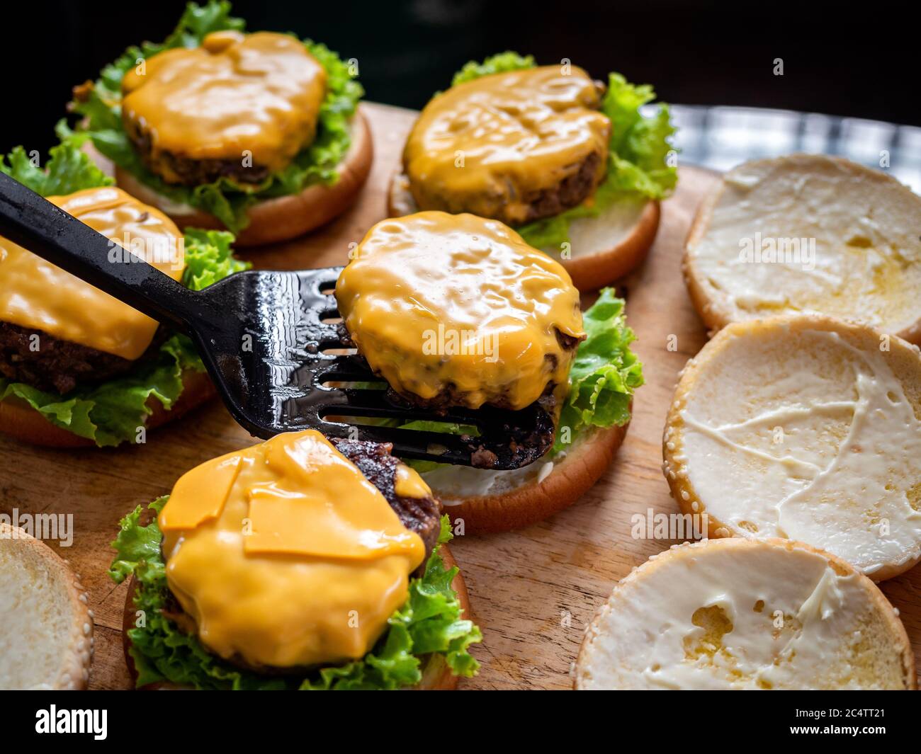Leckere hausgemachte saftige Burger. Hand mit Spatel Putting Beef Cover mit Käse auf frischen grünen Salat auf Holztisch, Prozess der Herstellung von köstlichen Hause Stockfoto