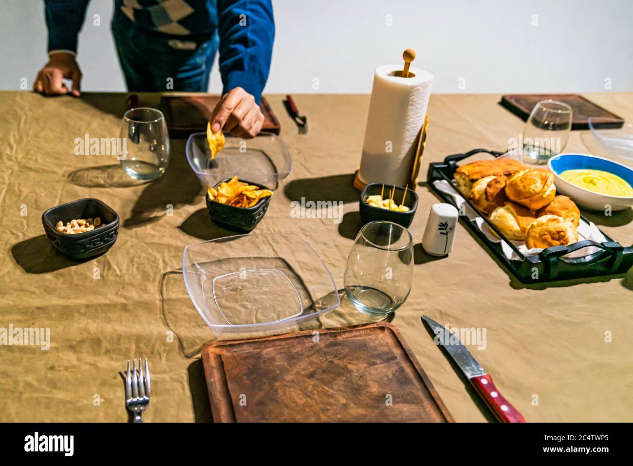 Mann hält pommes an einem Familientisch, der vorbereitet ist, um das Treffen von Freunden zu feiern, mit Saucen, Käse, Wein und Gerichten. Stockfoto