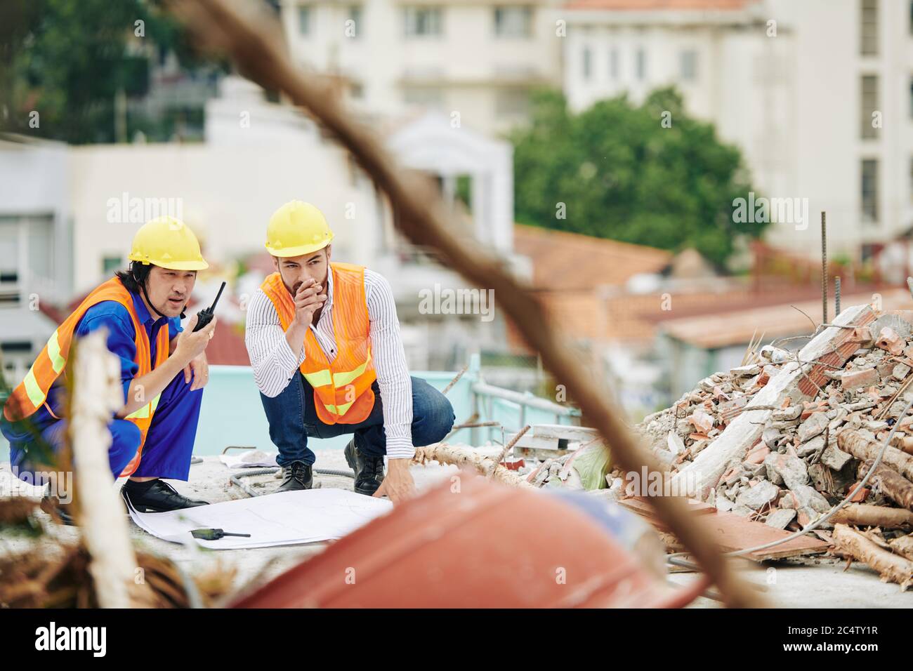 Ingenieure in leuchtend orangefarbenen Westen und Hüten diskutieren Arbeiten auf der Baustelle Stockfoto