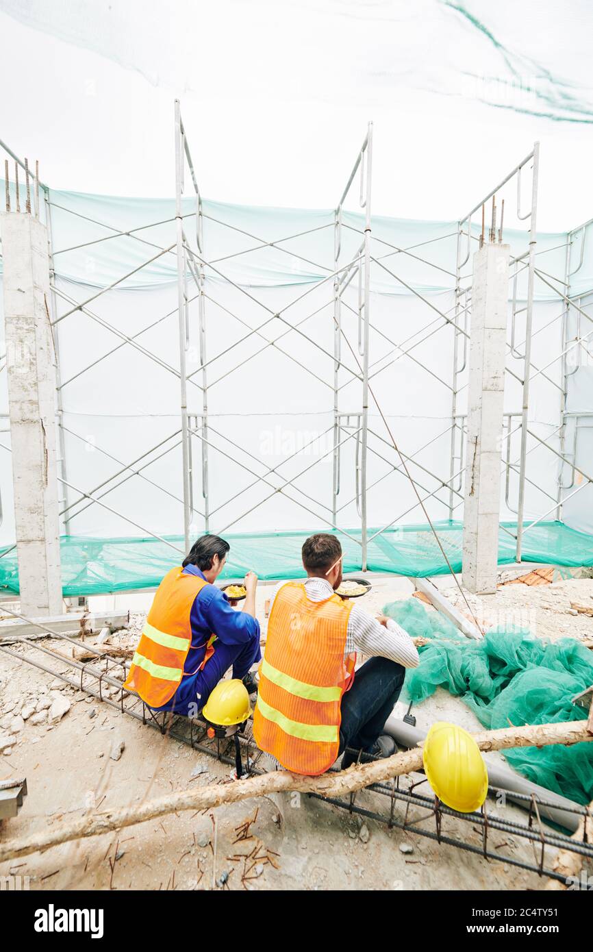 Bauleute in hellen Westen essen Mittagessen auf der Baustelle, Blick von hinten Stockfoto