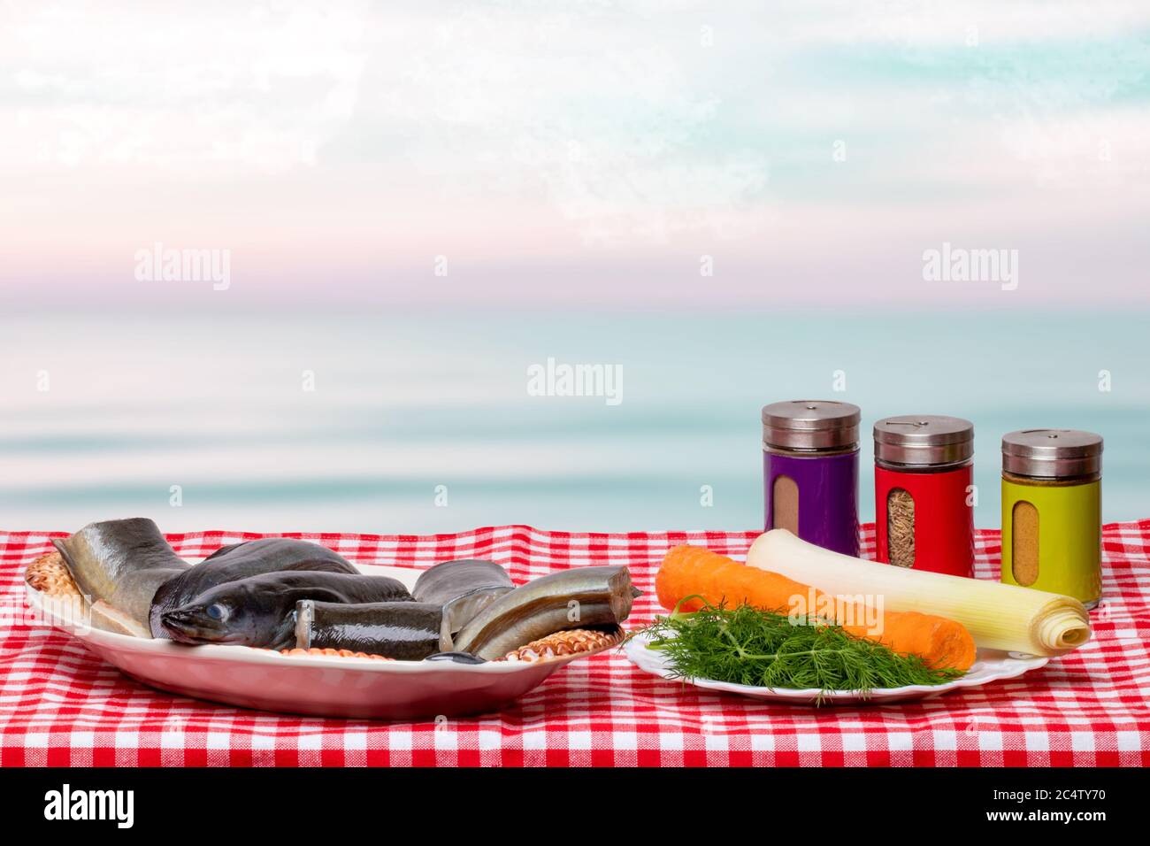 Nahaufnahme von frisch gereinigten Stücken rohen Aalfischs auf einem Porzellanteller und notwendigen Zutaten wie Gemüse, Gewürze und Gemüse für die Zubereitung Stockfoto