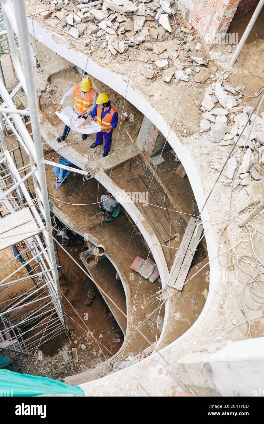 Bauingenieure in gelber Harthut diskutieren Bauplan bei der Arbeit vor Ort Stockfoto