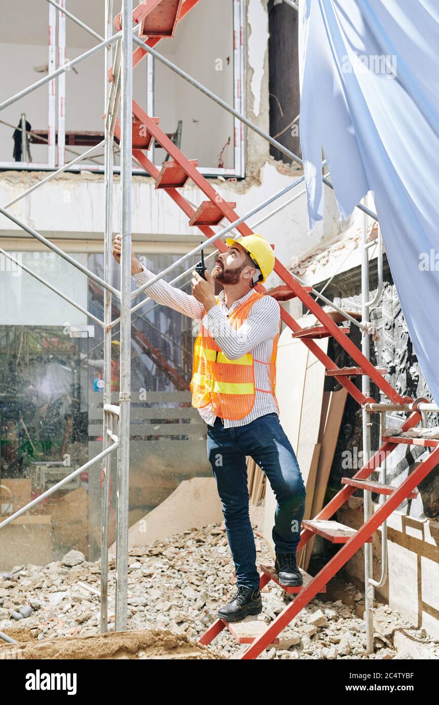 Auftragnehmer auf Leiter stehen und mit Walkie-Talkie, um die Arbeit der Bauherren auf dem Dach zu kontrollieren Stockfoto