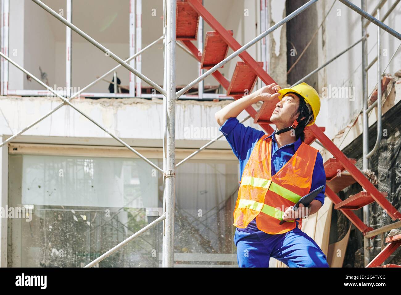 Bauarbeiter in orange Weste und Hardhat nach oben schauen und Bauherren auf dem Dach arbeiten zu überprüfen Stockfoto