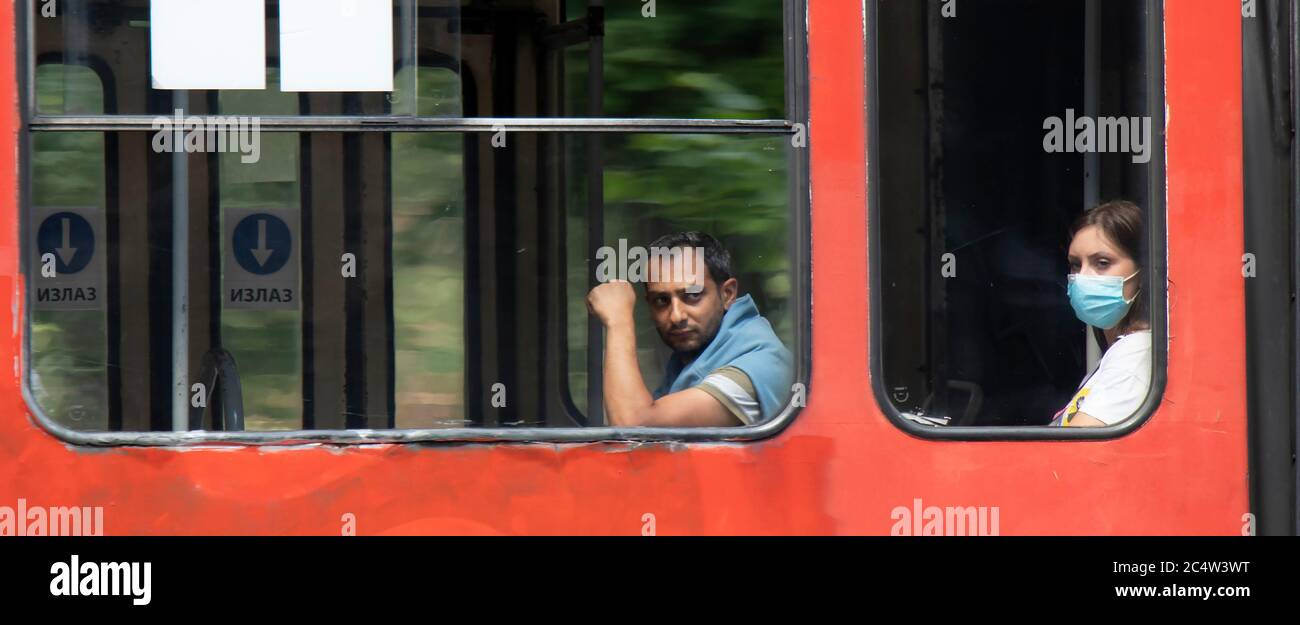 Belgrad, Serbien - 25. Juni 2020: Menschen mit chirurgischen Gesichtsmasken, während sie auf einem Fenstersitz einer fahrenden Straßenbahn sitzen und reiten, von außen Stockfoto