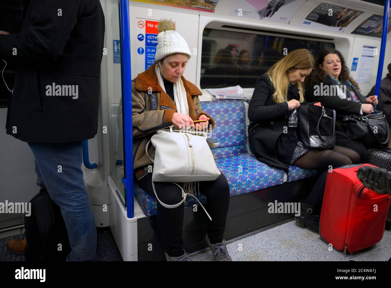 London, England, Großbritannien. Frau, die Musik auf ihrem Handy in einem U-Bahn-Zug hört Stockfoto