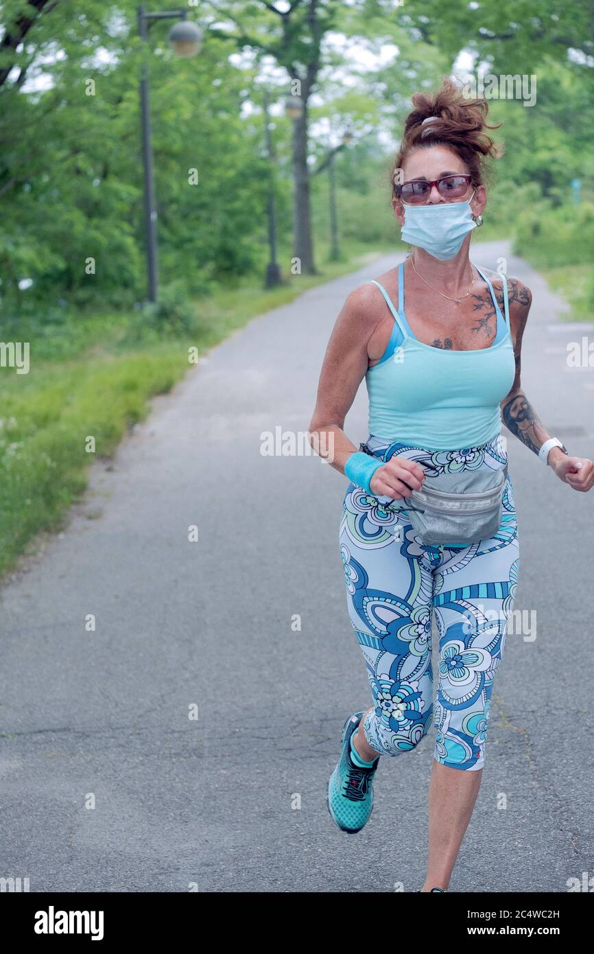 Eine attraktive Frau mittleren Alters, die auf dem Weg nahe der Bayside Marina läuft, während sie eine Maske über dem Mund trägt. In Bayside, Queens, New York. Stockfoto