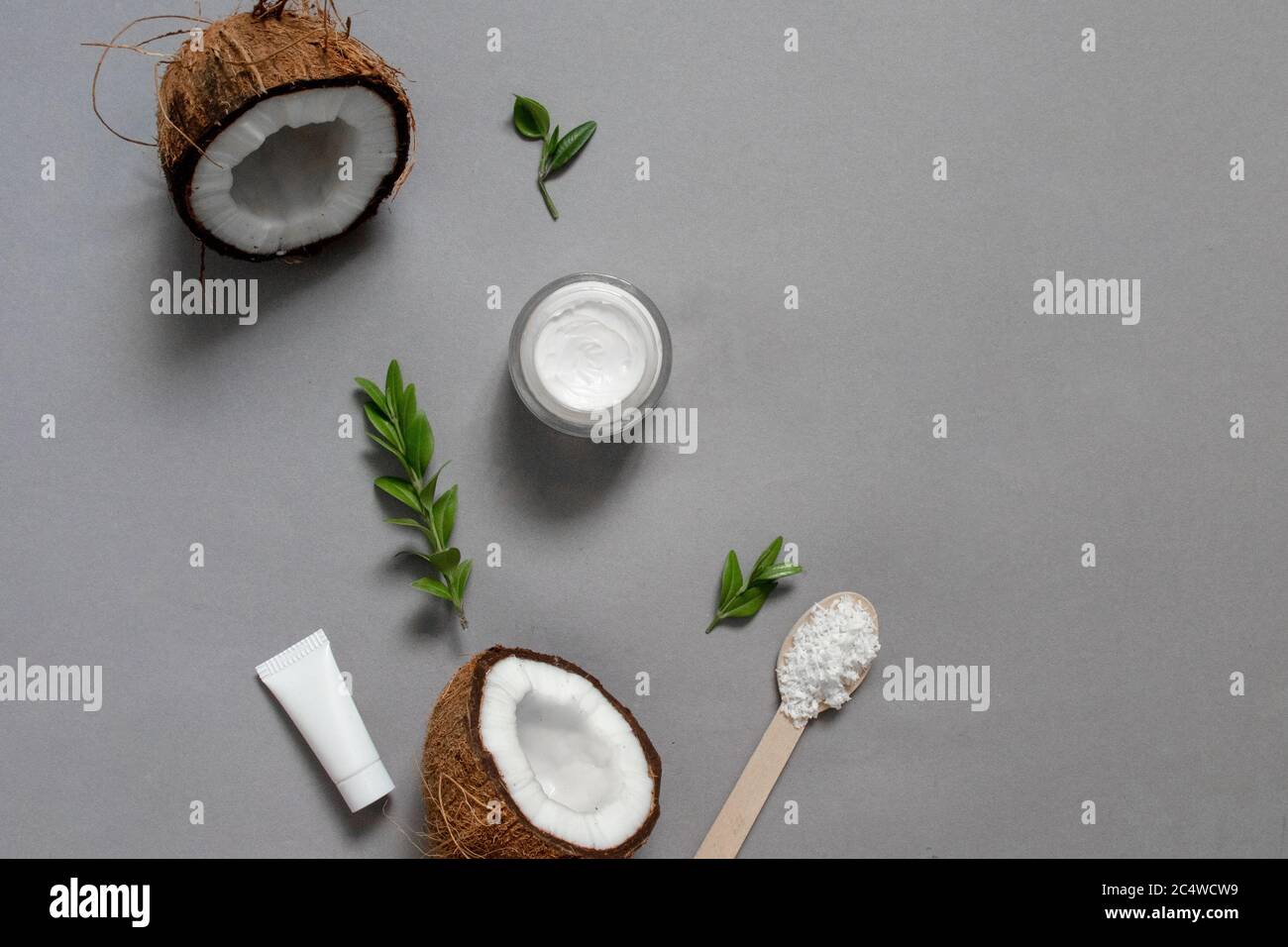 Hausgemachte Kokosöl Kosmetik für Haut und Haar Pflege. Öl in kleiner Flasche, Gesichtscreme, Kokosnusshälften mit Regal auf agray Hintergrund, Draufsicht Kopierraum Stockfoto