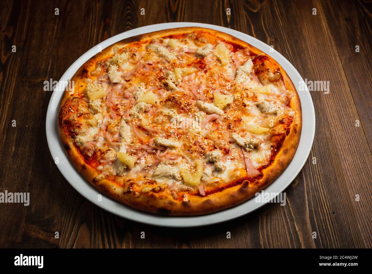 Schinken, Käse, Hühnerfleisch und Ananas Pizza, Holzhintergrund, Low-Key Stockfoto