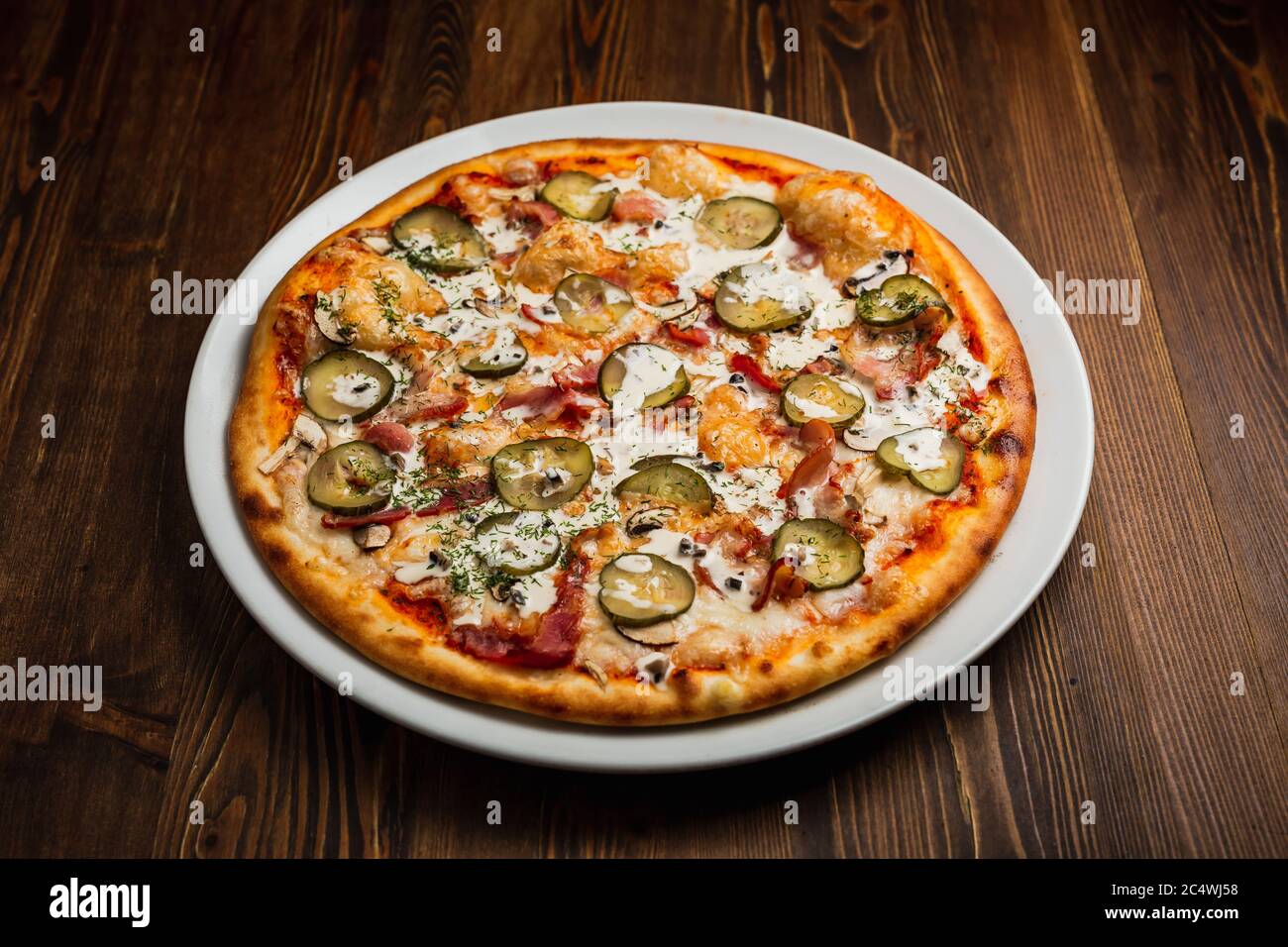 Speck, Pilze und Gurken nährende Pizza mit saurer Sahne-Sauce, Holzhintergrund, Low-Key Stockfoto