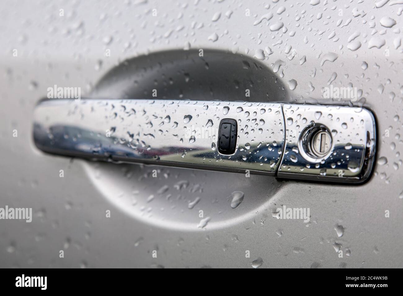 Verchromter Autotürgriff mit Schlüsselloch und Fernbedienung schlüssellose Öffnung Taste Abdeckung der Wassertropfen nach dem Regen, Seitenansicht Schärfe auf dem schwarzen Stockfoto