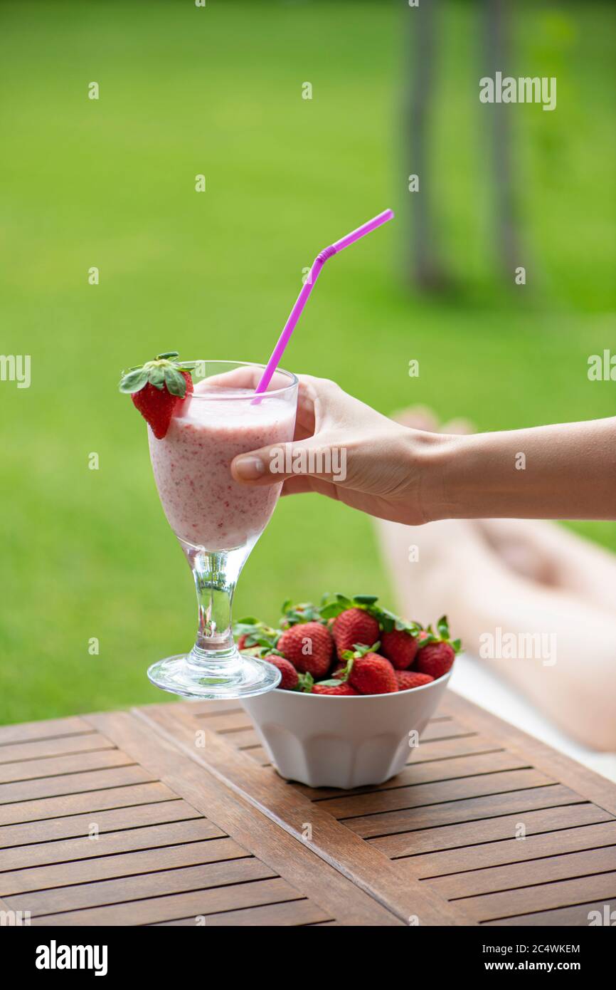 Frau auf einer Sonnenliege hält im Sommer einen Erdbeer-Smoothie neben einer Schüssel Erdbeeren Stockfoto