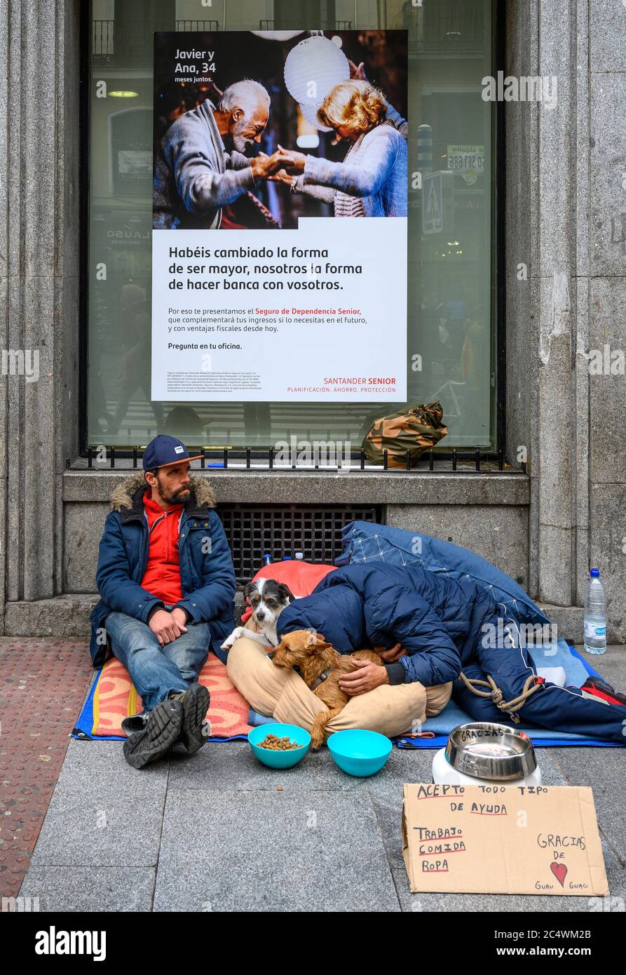 Obdachlose betteln mit ihren Haustieren, unterhalb einer Bankwerbung im Zentrum von Madrid, Spanien. Stockfoto