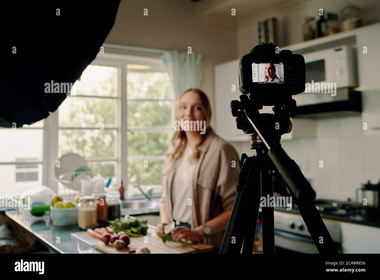 Fröhliche Lebensmittelbloggerin, die Video für Vlog bei der Kamera aufzeichnet, während sie in der modernen Küche steht Stockfoto