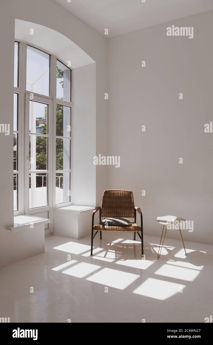 Leeres weißes, sonniges Zimmer mit Korbsessel und Tisch. Minimalistisches Design Stockfoto