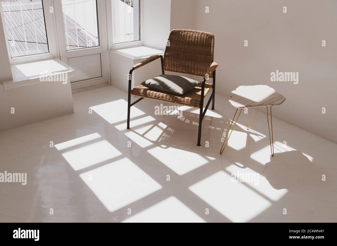 Leeres weißes, sonniges Zimmer mit Korbsessel und Tisch. Minimalistisches Design Stockfoto