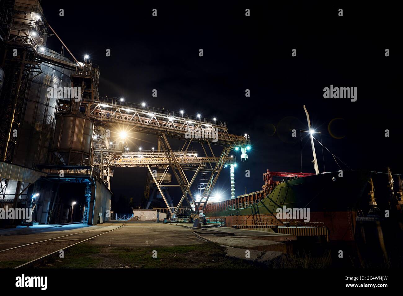 Großer Getreideanleger am Seehafen. Cerealien Massenumladung von der Straße zum Schiff in der Nacht. Beladen von Getreidepflanzen auf dem Schiff von großen Aufzügen bei Stockfoto