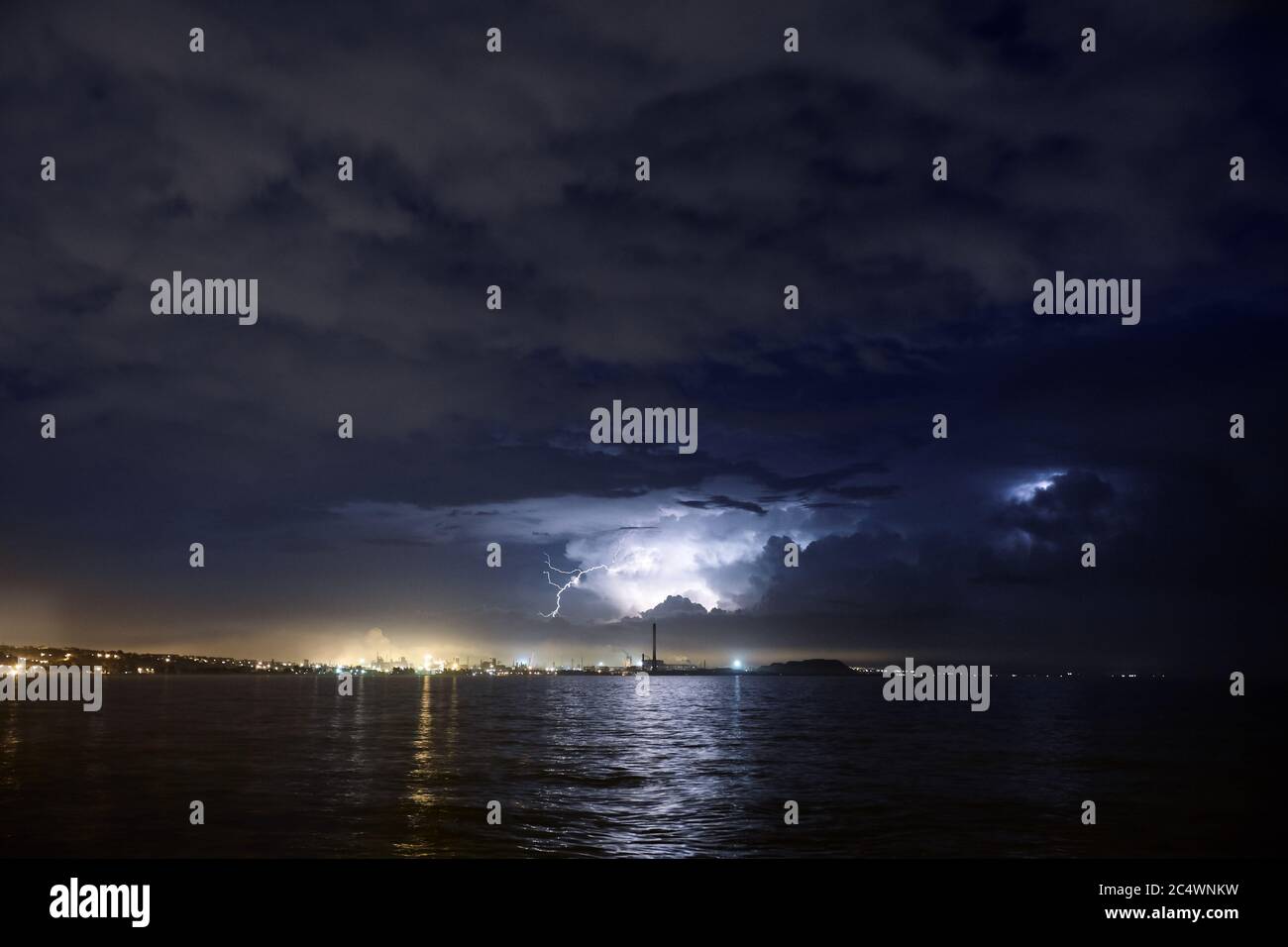Blitz über dem Meer oder See in der Nacht. Gewitter über der Skyline der großen Industriestadt. Stockfoto